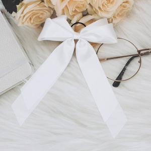 Close-up of elegant white satin ribbon bow hair clip on a soft white plush surface