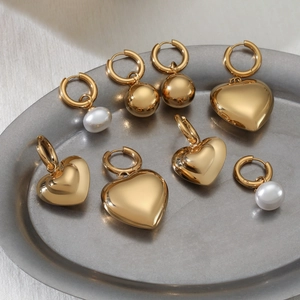 Polished gold stainless steel earrings set with pearl, heart and ball charms on tray