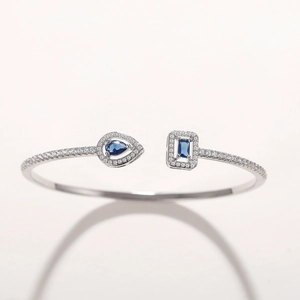 Detail view of silver open bangle featuring pear and rectangular blue zircons and crystals