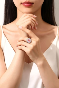 Close-up of an oval pink sapphire silver ring with white diamond accents on a finger