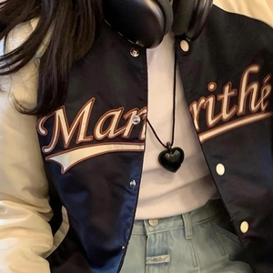 Gros plan d'un collier pendentif cœur noir porté par un mannequin en veste de baseball