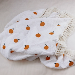 Detailed view of white cotton baby blanket with orange fruit print and fringe trim
