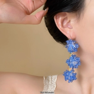 Detail of blue bead flower drop earrings worn, showing clear crystal texture and design