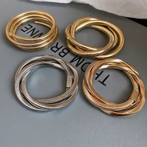 Set of spiral snake bone metal bangles in gold and silver finish on grey textured surface
