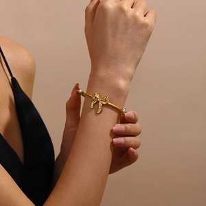 Gold-plated stainless steel open bangle with elegant bow design and white pearls