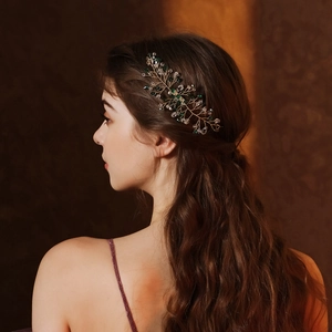 Detail of bridal hair comb with green crystal leaves and gold wire on model's hair