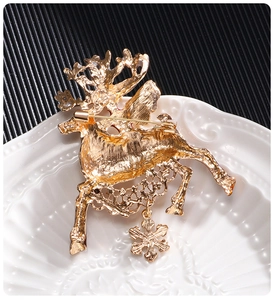 Close-up of golden reindeer brooch with snowflake pendant on white embossed plate