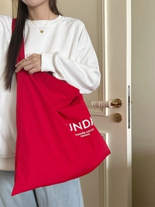 Large red canvas shoulder bag with white letter print shown in a stylish lifestyle setting