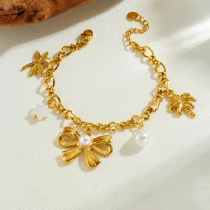 Golden charm bracelet with pearl, bow, dragonfly and palm tree pendants on white surface