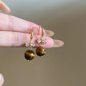 Macro view of gold bow earrings featuring zircon accents and brown tiger eye stone drops