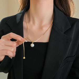 Detail of adjustable gold snake chain necklace with a white round pearl pendant on a model