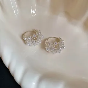Silver hollow lace hoop earrings with small white pearls on a minimalist ceramic plate