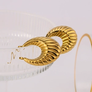 Close-up of golden U-shaped earrings with textured ribbing on a glass rim