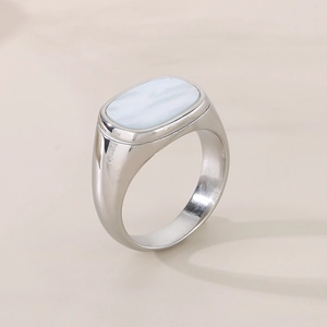 Close-up of silver stainless steel ring with white oval shell inlay on a beige background