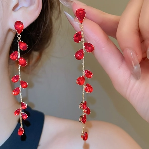 Detail of elegant gold drop earrings featuring red pear-cut crystals and long fringe tassels