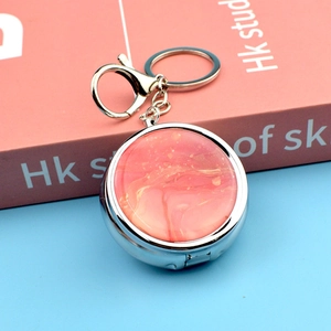 Detail of round metal pill box with coral marble pattern and secure key ring attachment