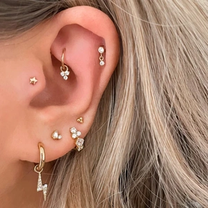 Close-up of gold layered ear piercings with star studs and lightning bolt dangles