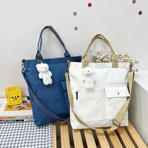 Detail of dark blue and off-white canvas bags with front pockets and plush bear charms