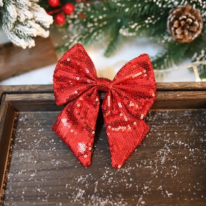 Sparkling red sequin Christmas bow decoration on a rustic wooden tray with pine cones