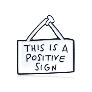Enamel brooch pin featuring This Is A Positive Sign humorous slogan in white and black