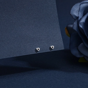 Close-up of elegant S999 silver hollow heart stud earrings on dark blue card display
