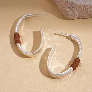 Detail of C-shaped geometric earrings with brown leather wrap on a stone base