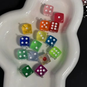 Close-up of colorful resin dice pendants with metal rings scattered on a white tray