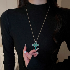 Détail d'un pendentif croix en cristal vert vintage avec chaîne dorée sur pull noir