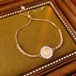 Vue détaillée du bracelet doré avec médaille religieuse en zircons sur un tissu tricoté vert