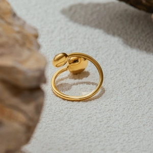 Artistic close-up of golden open ring with dual-bean design on white sand and rock background