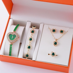 Detailed close-up of a golden jewelry set with green heart stones in an orange gift box
