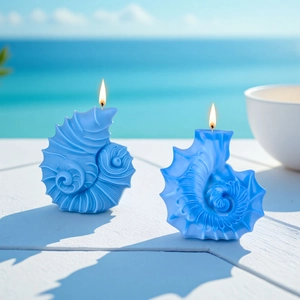 Two sky blue conch-shaped scented candles burning on a white wooden deck by the sea