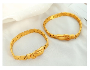 Detailansicht eines goldenen Armbands im Gürtelschnallen-Stil auf elegantem weißem Seidenstoff