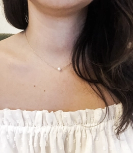 Close-up of minimalist gold choker necklace featuring a single white pearl on a model