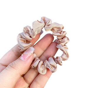 Champagne silk satin scrunchie with pleated design held by hand for hair care
