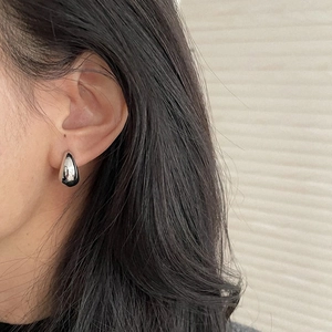Close-up of a silver teardrop earring in polished titanium steel worn on a model's ear