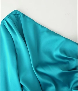 Détail de robe en satin bleu canard avec encolure à volants et texture soyeuse lisse