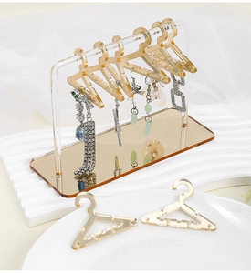Macro view of acrylic earring display stand with golden mini hangers on white ripple base