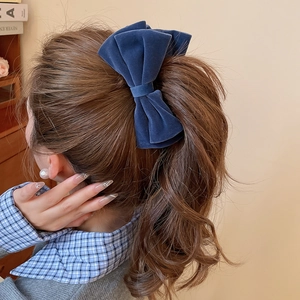 Detail of a large navy blue velvet bow hair clip worn on a ponytail for an elegant look