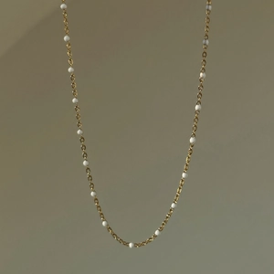 Detail of 18k gold plated necklace featuring delicate white enamel beads on a thin chain