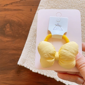 Detail of a yellow macaron padded bow hair tie secured on a card display