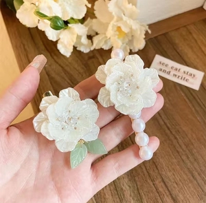 Detailed shot of white camellia hair clips with green leaves and pearls on wood background