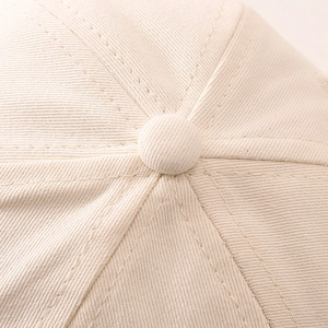 Gros plan du bouton supérieur et des coutures d'une casquette de baseball en coton crème