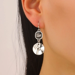 Close-up of geometric drop earrings with square dark crystal and hammered silver disc