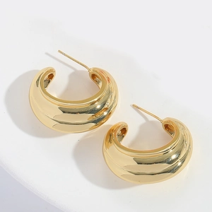 Close-up of golden chunky C-shaped hoop earrings with a polished mirror finish
