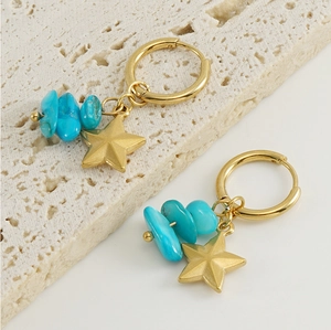 Detail of 18k gold star earrings with turquoise stones on a stone surface