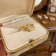 Detailed shot of a gold cross pattern ring with white stone in a beige velvet gift box