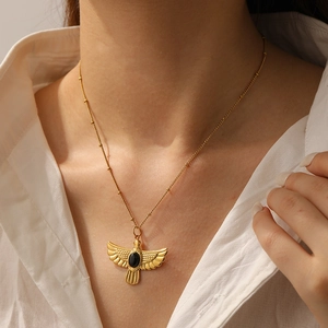 Detailed view of a gold bird pendant with an oval black stone on a fine chain necklace