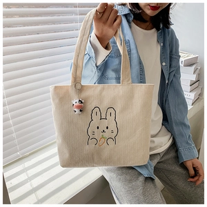 Detail of beige corduroy tote bag featuring a cute embroidered rabbit and charm