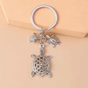 Retro silver turtle keychain with hollow shell and small charms on beige surface